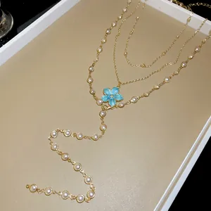 Close-up of a layered gold necklace with pearls and a blue floral pendant detail
