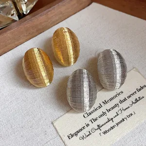 Macro detail of gold and silver oval stud earrings with horizontal ribbed texture