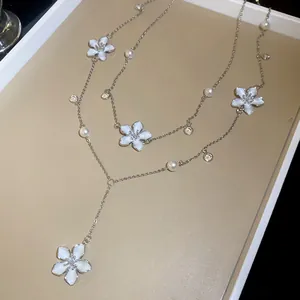 Detailed macro view showing the fine white enamel flower charms and pearls on a silver chain