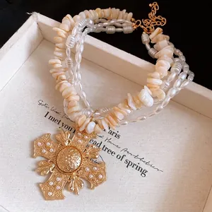 Elegant multi-layer necklace with pearl and shell chips featuring a large ornate gold cross