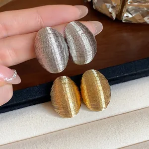 Detail of textured oval stud earrings in gold and silver tones with ribbed surface