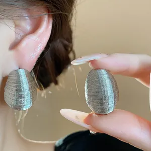 Close-up view of elegant silver oval stud earrings featuring a fine ribbed winding pattern