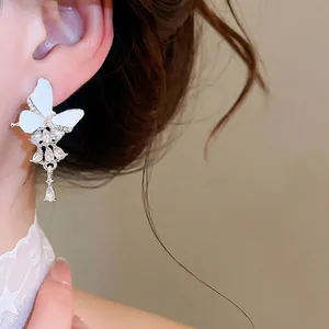 Elegante Schmetterlings-Ohrstecker mit weißer Emaille und Strass-Quasten am Ohr.