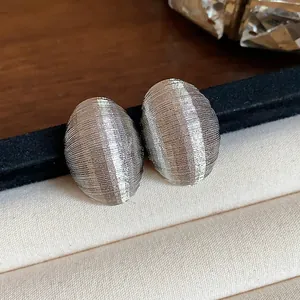Macro view of silver-toned oval stud earrings featuring a fine ribbed texture detailing.