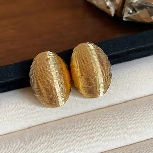 Close-up detail of golden minimalist oval stud earrings with fine ribbed texture