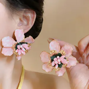 Detailed macro view of large pink enamel flower earrings with golden edges and pearls.