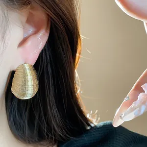 Close-up of gold textured oval stud earrings with elegant silver needles shown on ear.