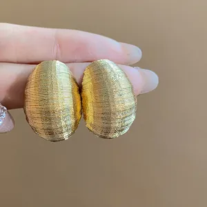 Detailed macro view of gold-toned textured oval stud earrings with wire-wrap design