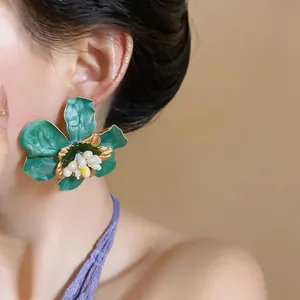 Detailed view of green enamel flower stud earring with gold edges on model's ear