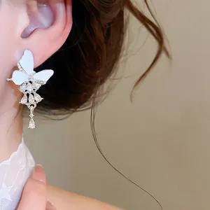 Nahaufnahme eleganter weißer Schmetterling-Quastenohrringe mit funkelnden Strasssteinen