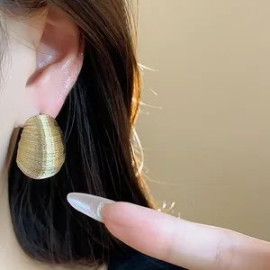 Macro detail view of elegant gold oval stud earrings with fine ribbed texture on model ear