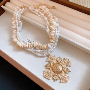 Close-up of multi-layer pearl and shell necklace with ornate gold cross pendant