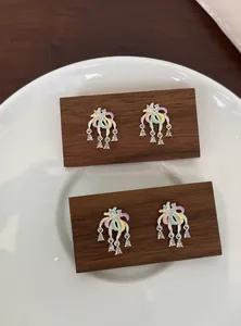Dettaglio di orecchini a fiore colorati con strass su blocchi di legno scuro eleganti.