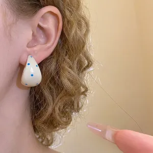 Elegant cream white C-shaped hoop earrings with blue polka dots worn on model ear