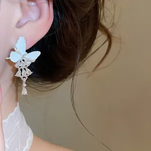 Nahaufnahme von weißen Schmetterlings-Ohrringen mit glitzernden Strasssteinen am Ohr.