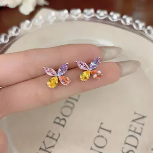 Detailed close-up view of colorful butterfly-shaped zircon flower stud earrings on fingers
