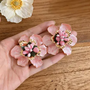 Close-up of pink enamel flower earrings featuring intricate gold stamen and textured petals.