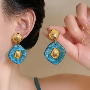 Close-up of blue marble resin earrings with gold textured diamond studs and elegant finish