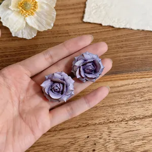 Dettaglio ravvicinato di eleganti orecchini a lobo a forma di rosa viola nella mano