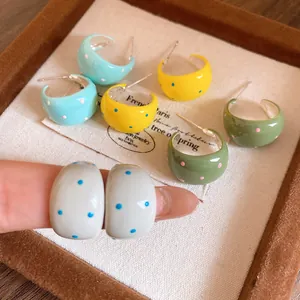 Close-up detail of colorful polka dot C-shape enamel earrings displayed on a tray
