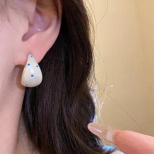 Close-up detail of white enamel C-shape stud earrings with blue polka dots on the ear