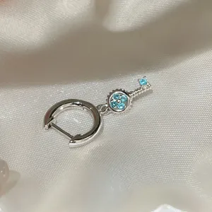 Detailed close-up of a silver hoop earring featuring a key pendant with light blue zircons