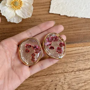 Dettaglio ravvicinato di eleganti orecchini in resina con vere fette di fiori secchi rosa