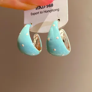 Close-up of light blue enamel C-shape hoop earrings with white polka dots design