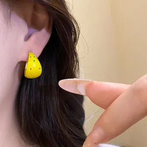 Detail shot of yellow C-shaped stud earrings with blue polka dots on ear.