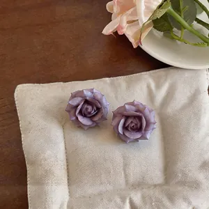 Dettaglio ravvicinato di orecchini a rosa 3D viola su un morbido cuscino color crema