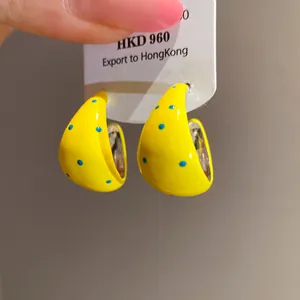 Close-up detail of yellow enamel C-shaped earrings featuring blue polka dots and silver pins