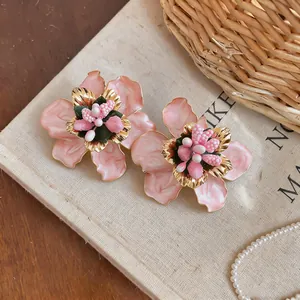 Macro view showing detailed pink enamel flower earrings with golden accents.