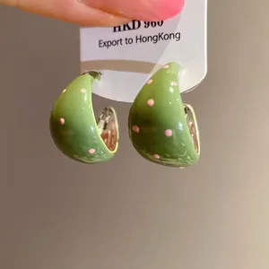 Close-up detail of green enamel C-shaped hoop earrings featuring pink polka dot patterns