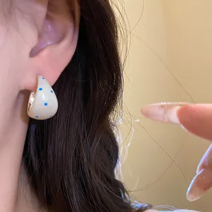 Macro detail shot of cream enamel C-shape hoop earrings with blue polka dots on a model's ear