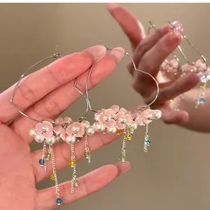 Nahaufnahme von herzförmigen Creolen mit rosa Blumen und bunten Perlenquasten