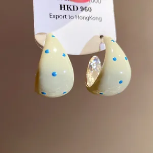 Detailed view of cream C-shaped hoop earrings with blue polka dot enamel finish.