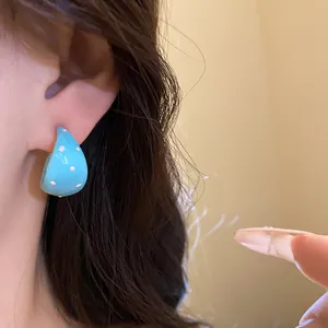 Close-up detail of a bright blue C-shaped enamel earring with white polka dots worn on ear