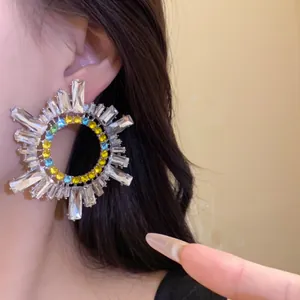 Gros plan détaillé de boucles d'oreilles soleil géométriques avec strass colorés sur l'oreille.