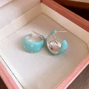 Close-up of light blue enamel C-shaped hoop earrings with white polka dots in a pink box.