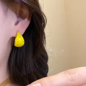 Close-up detail view of yellow C-shaped hoop earring with blue polka dot enamel finish