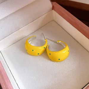 Close-up of yellow polka dot C-shape enamel earrings displayed in a pink gift box