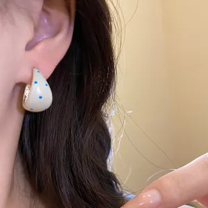 Close-up of polka dot C-shaped stud earrings with cream finish and blue dots