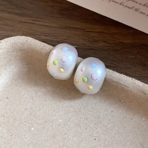 Dettaglio di orecchini a perno ovali opachi con pois colorati su un supporto materico