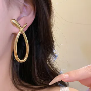 Detailed close-up showing glossy gold hollow crossover earrings worn on a model's ear
