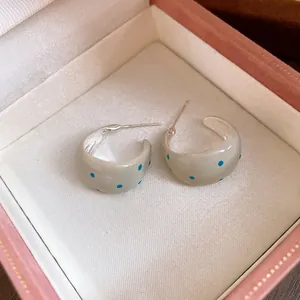 Detailed view of cream enamel C-shaped earrings with blue polka dots in a pink jewelry box