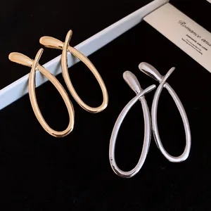 Detail view of large minimalist crossed hollow earrings in gold and silver finishes.