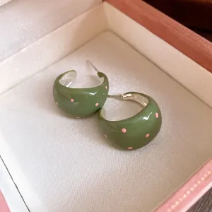 Macro detailed view of vintage green enamel C-shaped stud earrings with pink polka dots