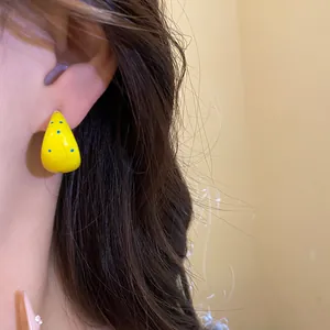 Close-up detail of vibrant yellow C-shaped enamel earrings with playful blue polka dots