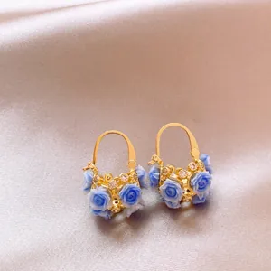 Close-up of elegant gold basket earrings featuring blue roses and zircon stones on satin