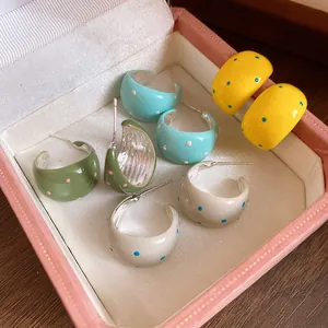 Detailed view of colorful enamel polka dot C-shaped hoop earrings in a jewelry box